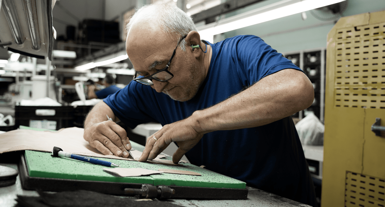 Bota sendo costurada à mão em bancada de oficina artesanal